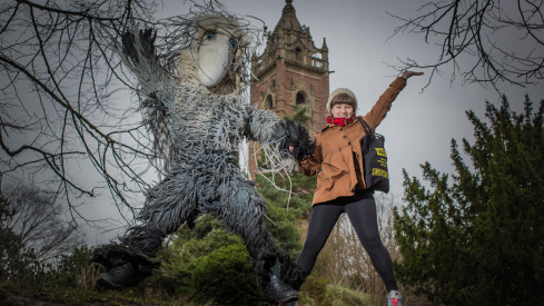 A female and a furry character jump in the air whilst holding hands